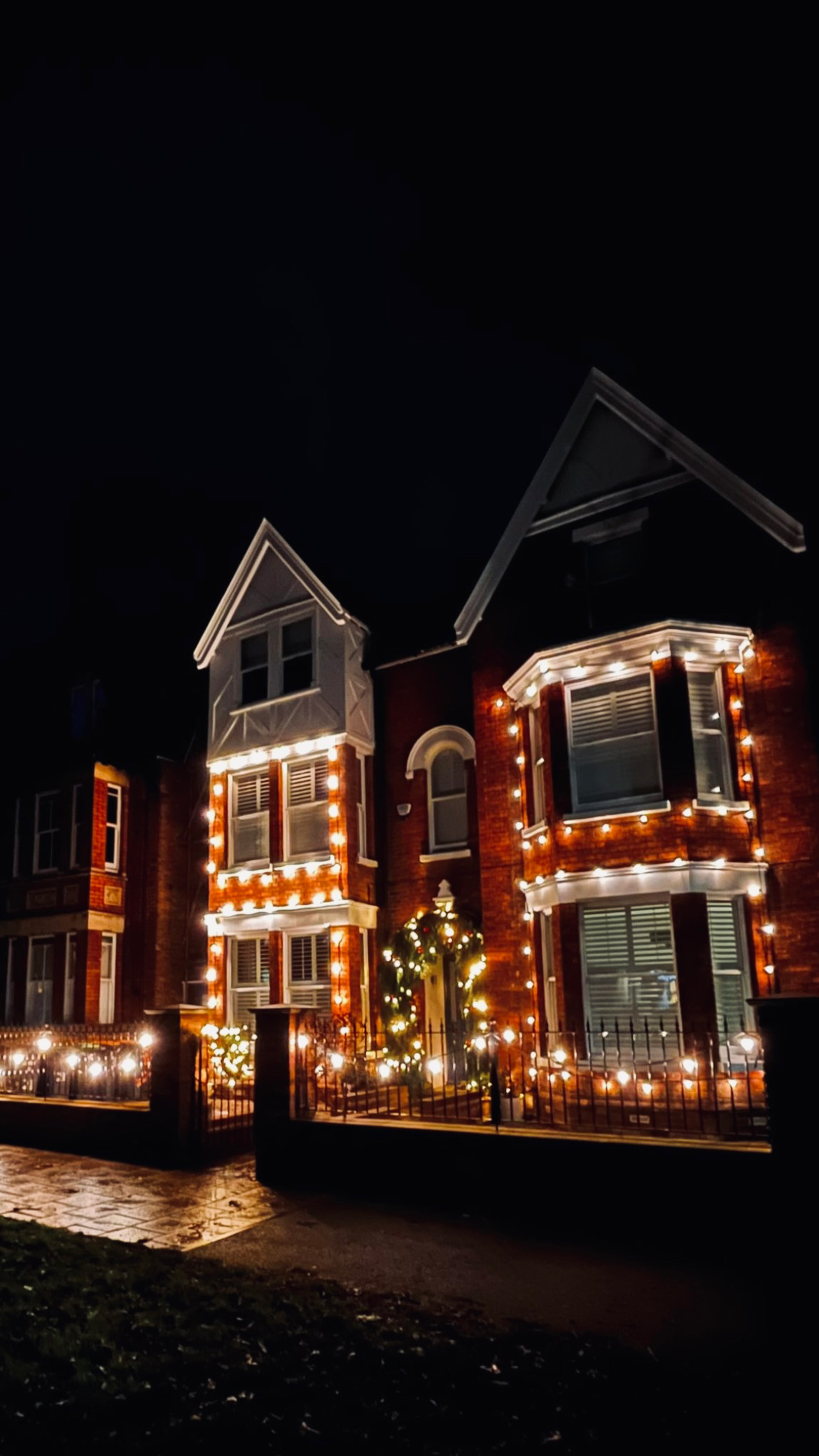Victorian house outlined in warm Christmas lights with wreath at entrance