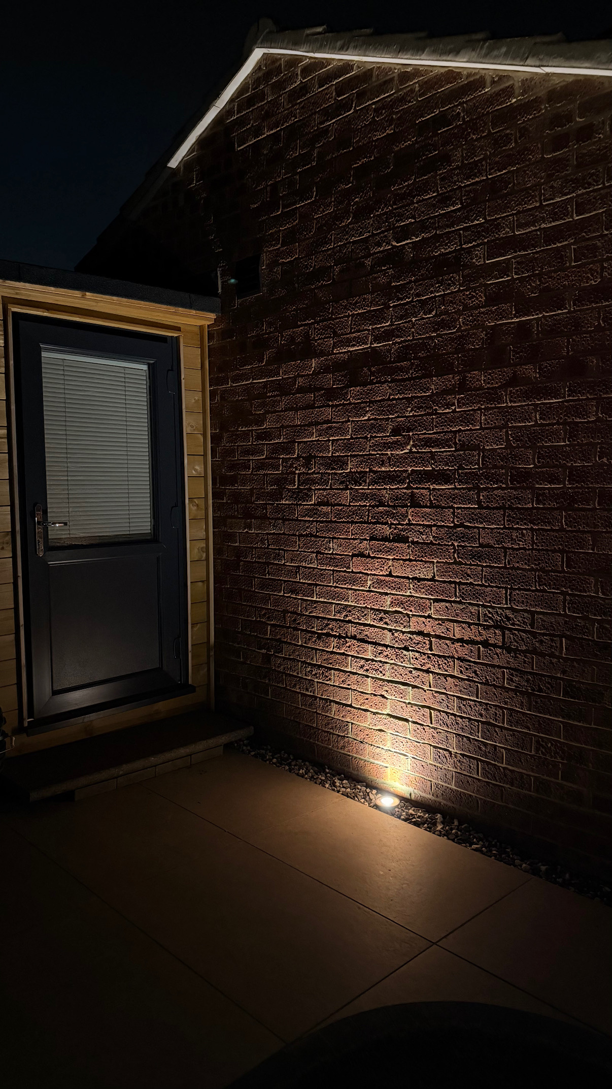 Uplit brick wall beside a garden room entrance at night
